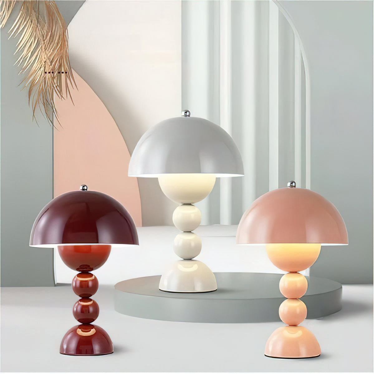 Wine red, white and pink Clérachic dome lamps stand at different heights on a grey platform before a pale arched backdrop.