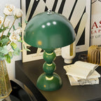 A green Clérachic dome lamp on a black desk, beside an open book, reading glasses, white roses and a graphic poster.
