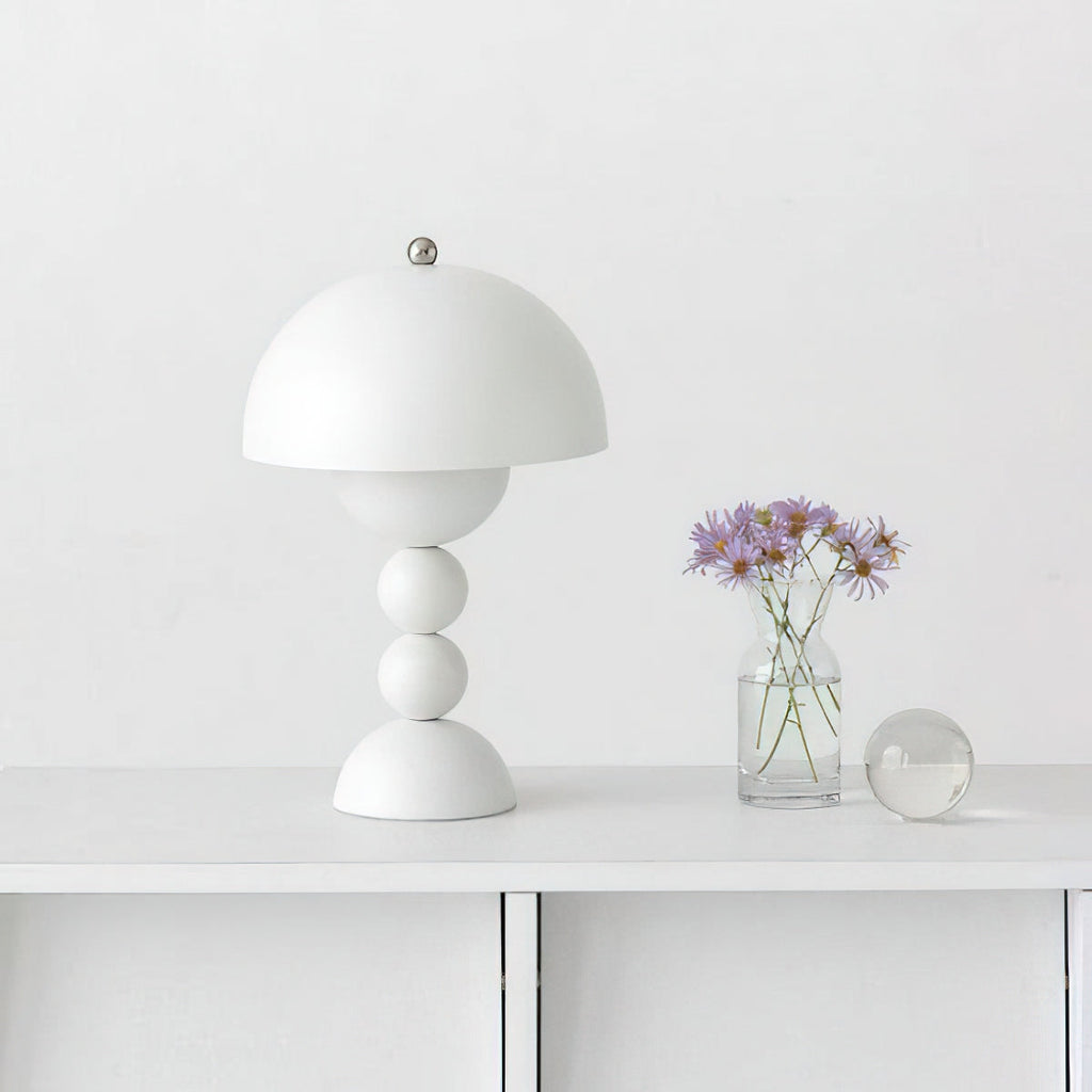 A white Clérachic dome lamp on a white console beside a small glass vase of purple flowers and a glass ball.