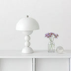 A white Clérachic dome lamp on a white console beside a small glass vase of purple flowers and a glass ball.