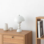 Small white Clérachic dome lamp on a wooden cabinet, with a ribbed vase, a small pot and books on a shelf nearby.