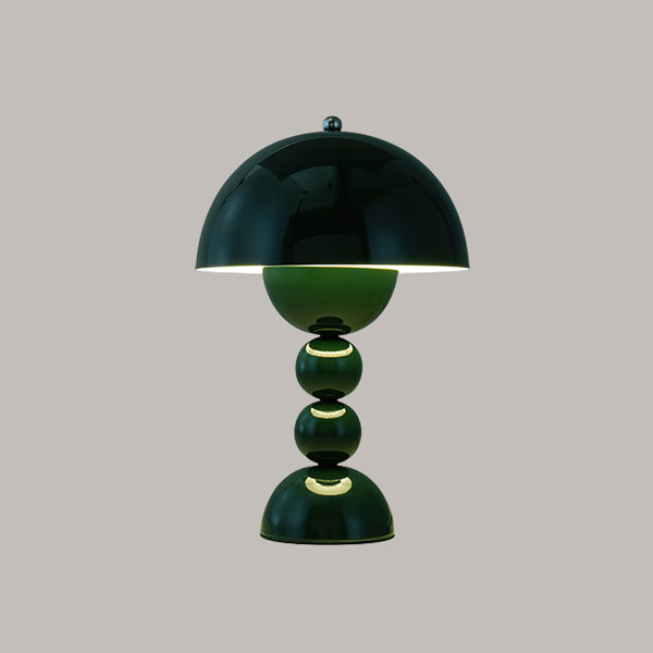 A dark green glossy Clérachic dome lamp with stacked spheres and a lit centre, on a grey backdrop.