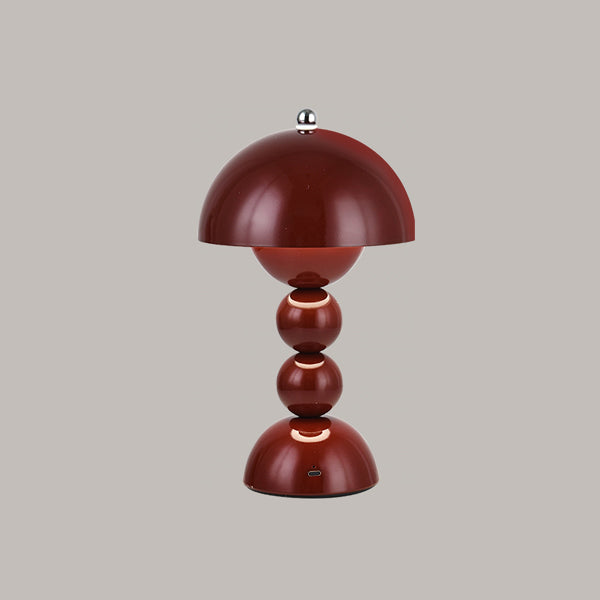 Wine red Clérachic dome lamp with glowing rings between its spheres and a charging port on the base, on grey.