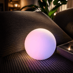 The Clérachic orb lamp lit pink on a corduroy sofa cushion beside a trailing plant.