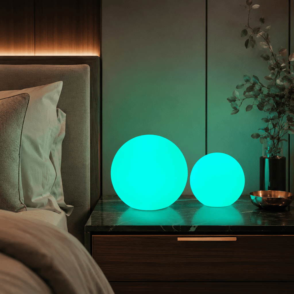 Two Clérachic orb lamps glowing turquoise on a marble nightstand beside a made bed.