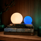 Clérachic orb lamps in warm white and blue, lit on a stack of art books against walnut.