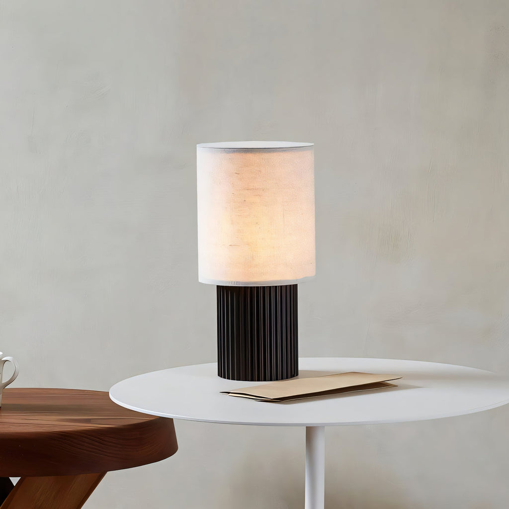Lit linen shade of this Clérachic table lamp on a small white round table, against a soft plaster-coloured wall.