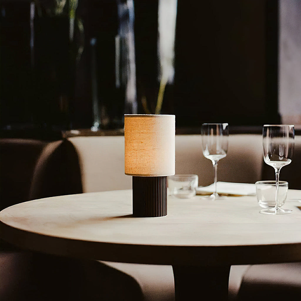 Dusk scene with this Clérachic table lamp lit on a round restaurant table, wine glasses and a curved banquette behind it.