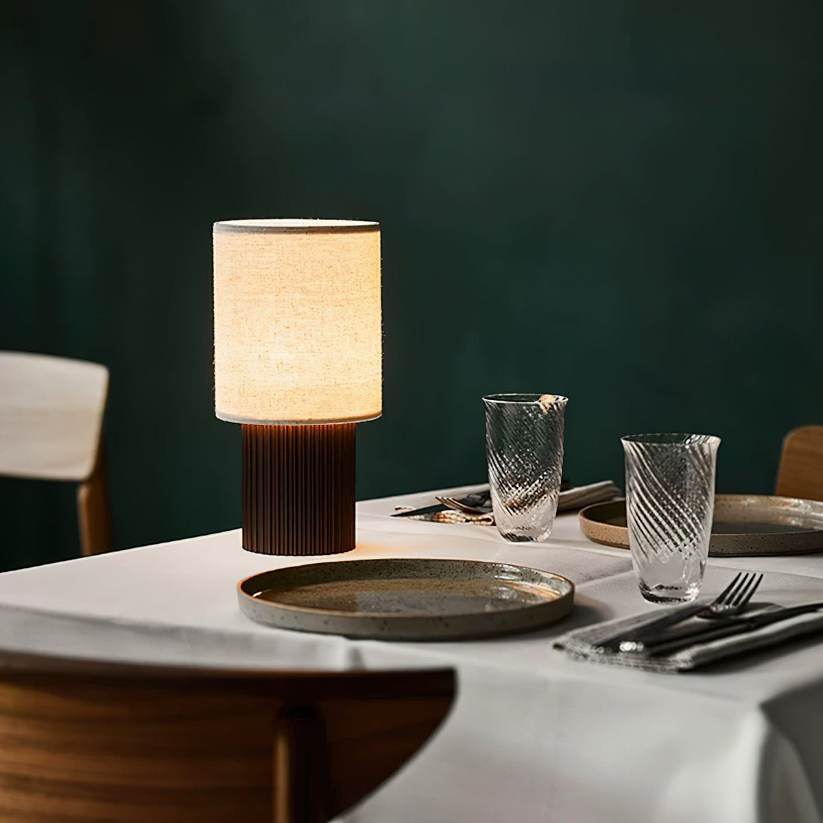 This Clérachic ribbed-base lamp glows on a set dining table against a deep green wall, with plates and cutlery beside it.
