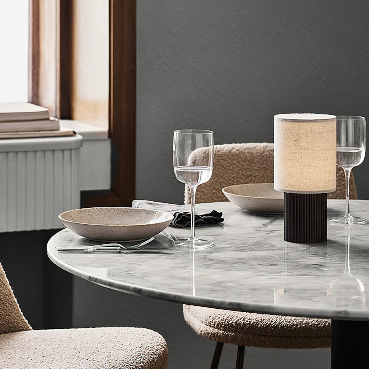 Beside a wine glass on a marble-topped round table, this Clérachic lamp shows its pale linen shade and ribbed brown base.