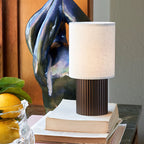 Close framing of this Clérachic lamp on a stack of books, with a glossy blue sculpture and a lemon bowl beside it.