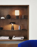 Lit in a dark oak wall niche, this Clérachic lamp sits on a shelf above books, with a small mushroom lamp below.