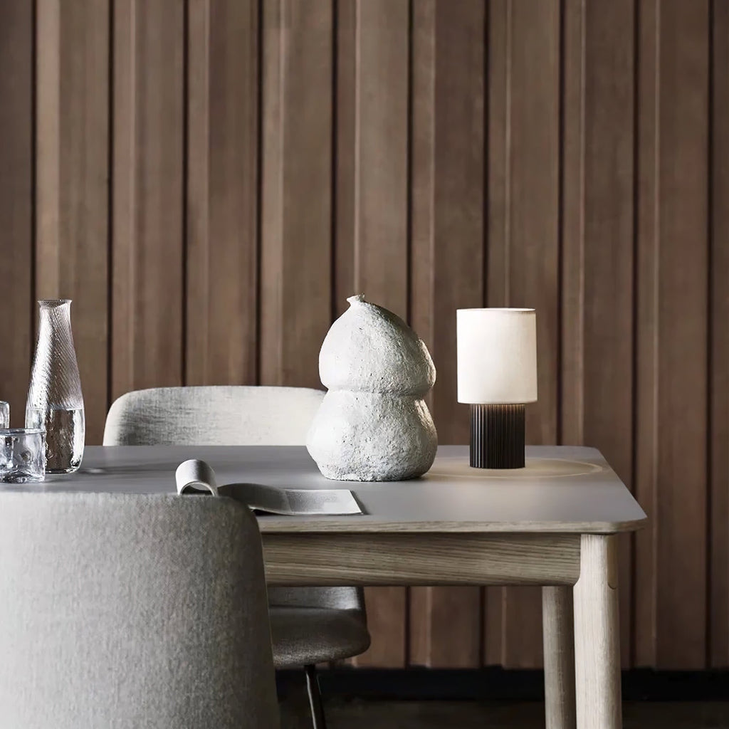 Wider view of this Clérachic lamp on a light table in front of panelled timber, an open magazine and a vase beside it.