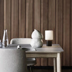 Wider view of this Clérachic lamp on a light table in front of panelled timber, an open magazine and a vase beside it.