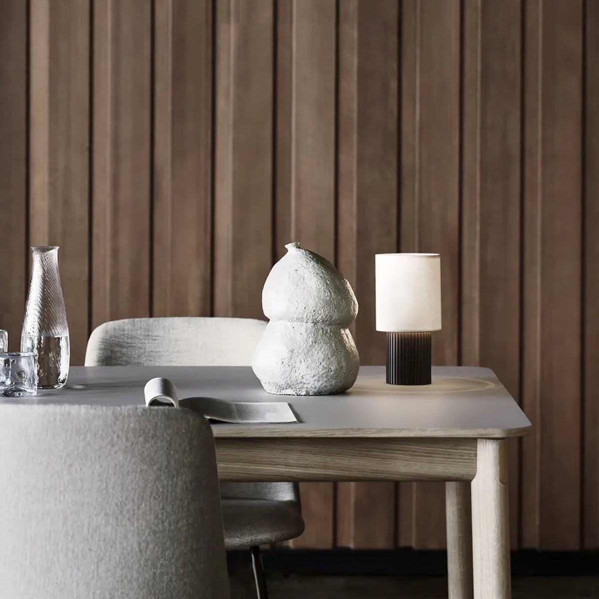 Wider view of this Clérachic lamp on a light table in front of panelled timber, an open magazine and a vase beside it.