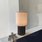 This Clérachic table lamp on a white sideboard, its lit linen shade and ribbed brown base seen close against a pale wall.