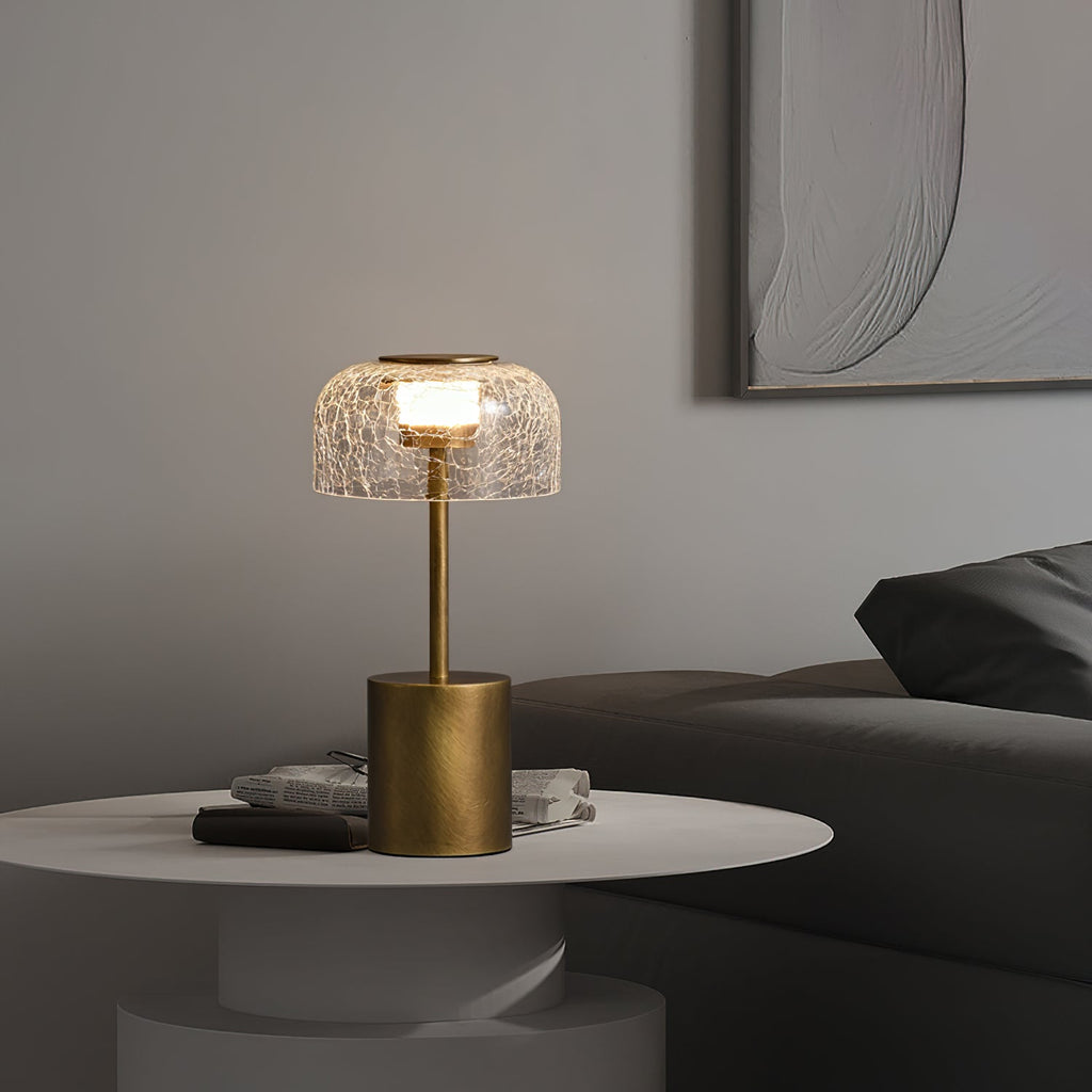 Lit crackle glass table lamp from Clérachic on a round white side table with magazines, in front of a grey sofa and a textured wall panel.