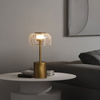 Lit crackle glass table lamp from Clérachic on a round white side table with magazines, in front of a grey sofa and a textured wall panel.