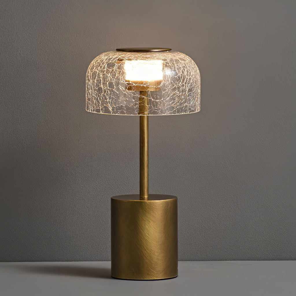 Close view of the lit crackle glass dome and bronze stem of this Clérachic table lamp, against a grey wall.
