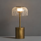 Close view of the lit crackle glass dome and bronze stem of this Clérachic table lamp, against a grey wall.