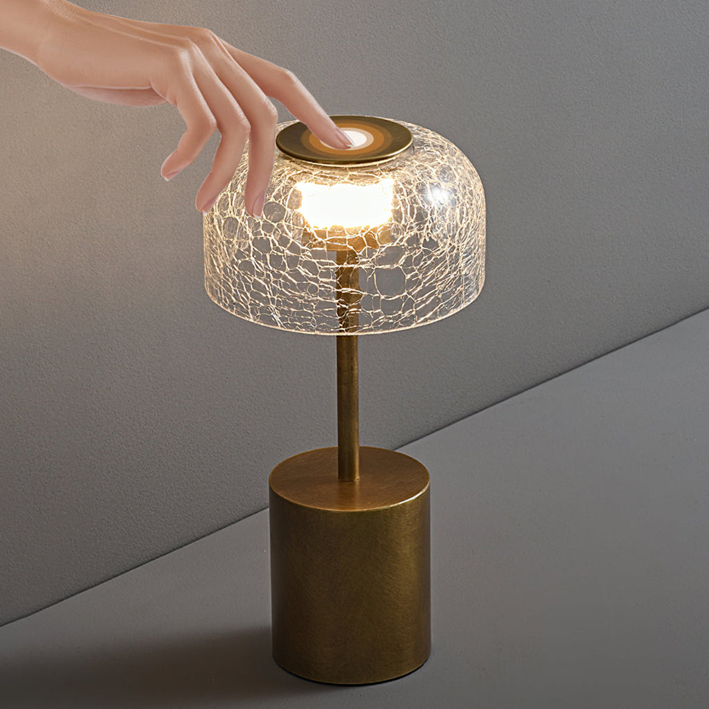 Lit crackle glass lamp from Clérachic on a wooden console, with books, dark candles and heavy curtains behind.