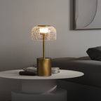 Clérachic crackle glass table lamp lit on a white round table, with a pile of magazines and a dark sofa behind.