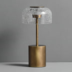 Unlit crackle glass dome on a bronze stem and round base, from Clérachic, against a grey wall.