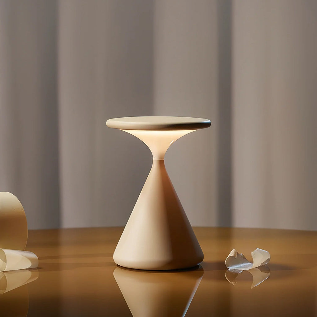 A Clérachic cordless table lamp glowing under its flat disc top, standing on a polished wooden table in front of grey curtains.