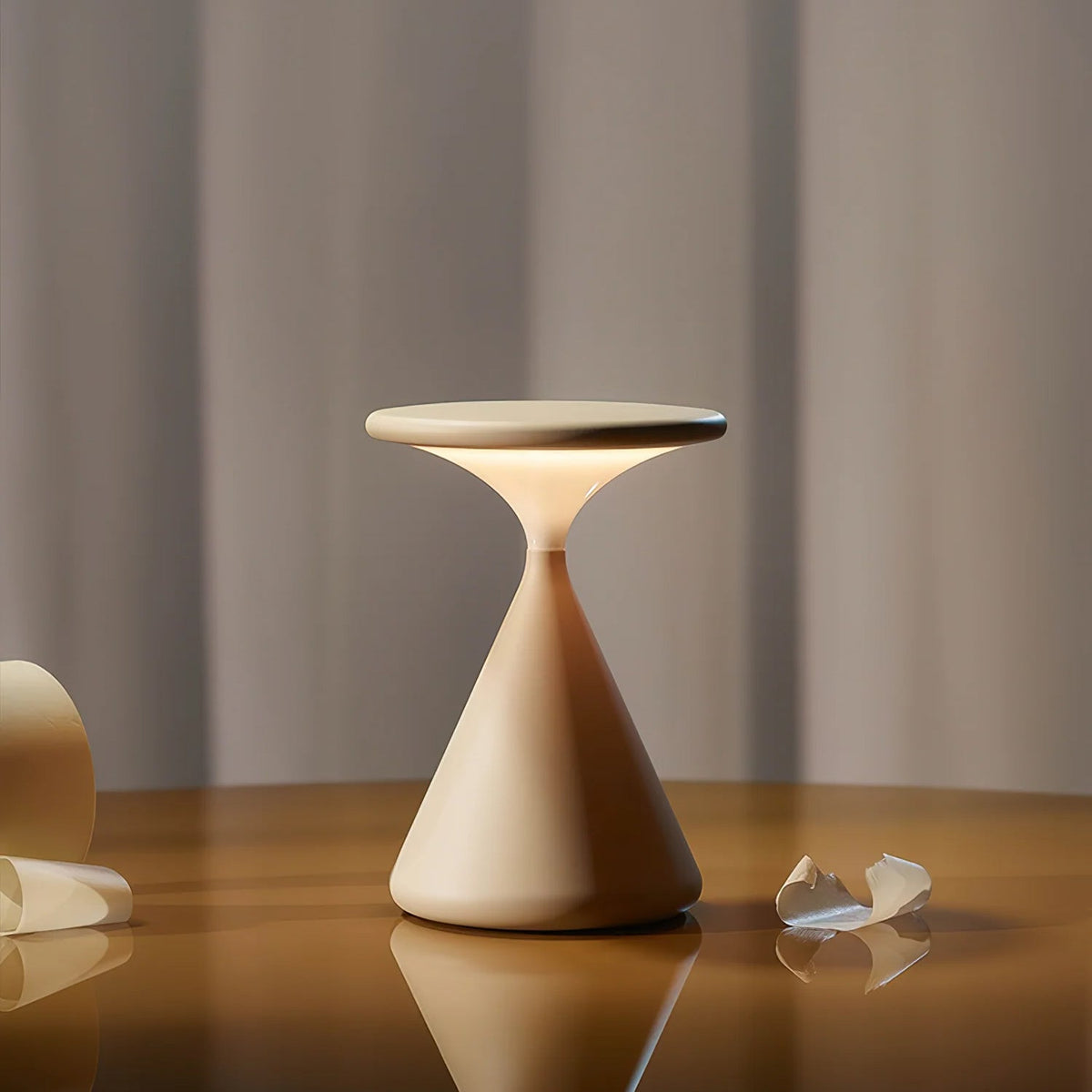 A Clérachic cordless table lamp glowing under its flat disc top, standing on a polished wooden table in front of grey curtains.