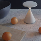 Cream Clérachic table lamp, unlit, on a speckled stone surface beside two oranges and a pale wooden board.