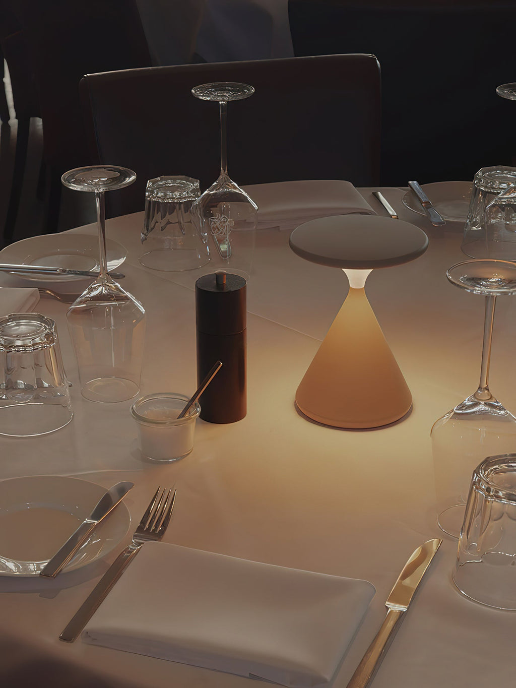 A brown Clérachic table lamp lit among glasses, cutlery and a pepper mill on a restaurant table.