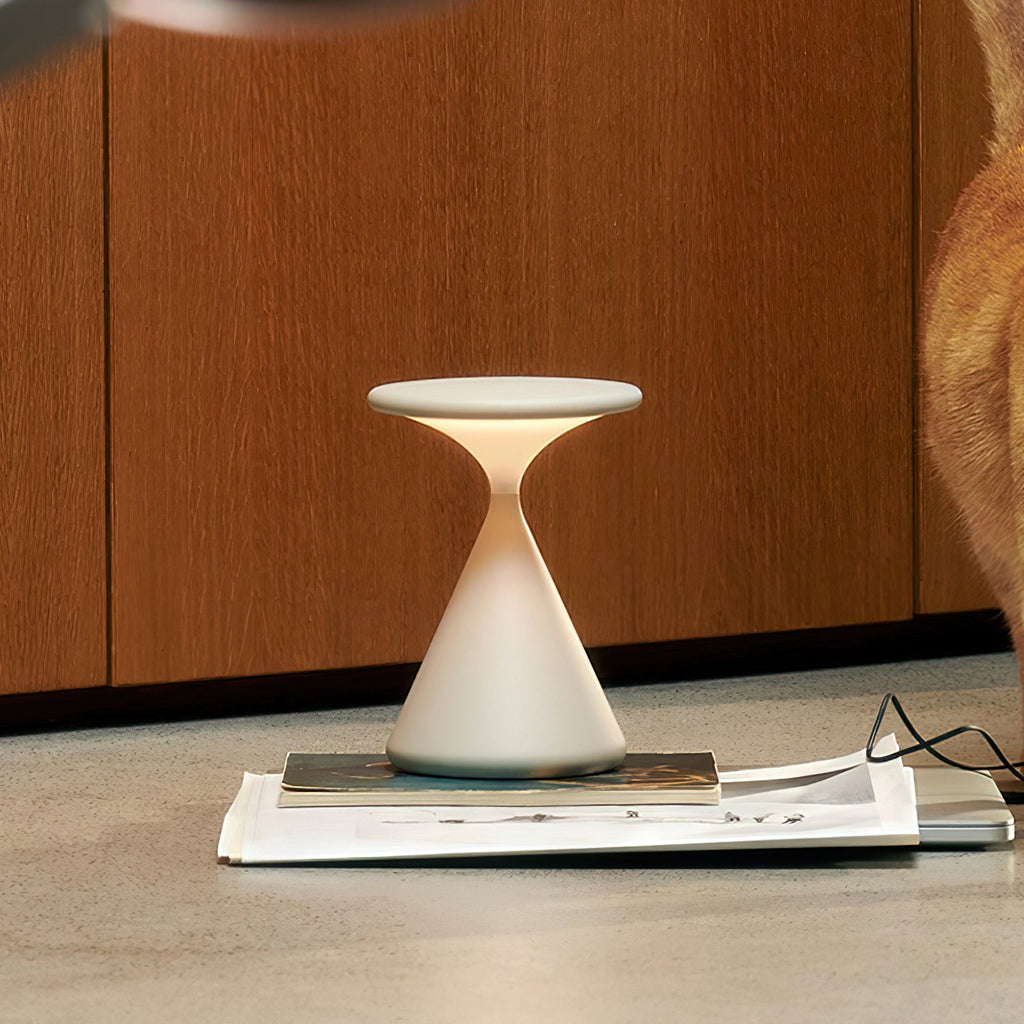 A cream Clérachic table lamp lit on a magazine on the floor, in front of wooden cabinet doors.