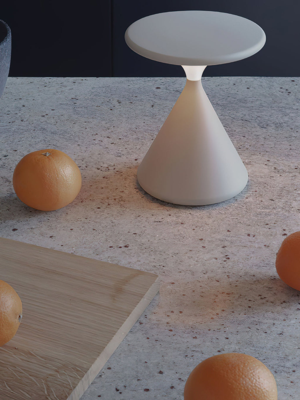 Cream Clérachic table lamp, unlit, on a speckled stone surface with oranges around it, in a portrait crop.