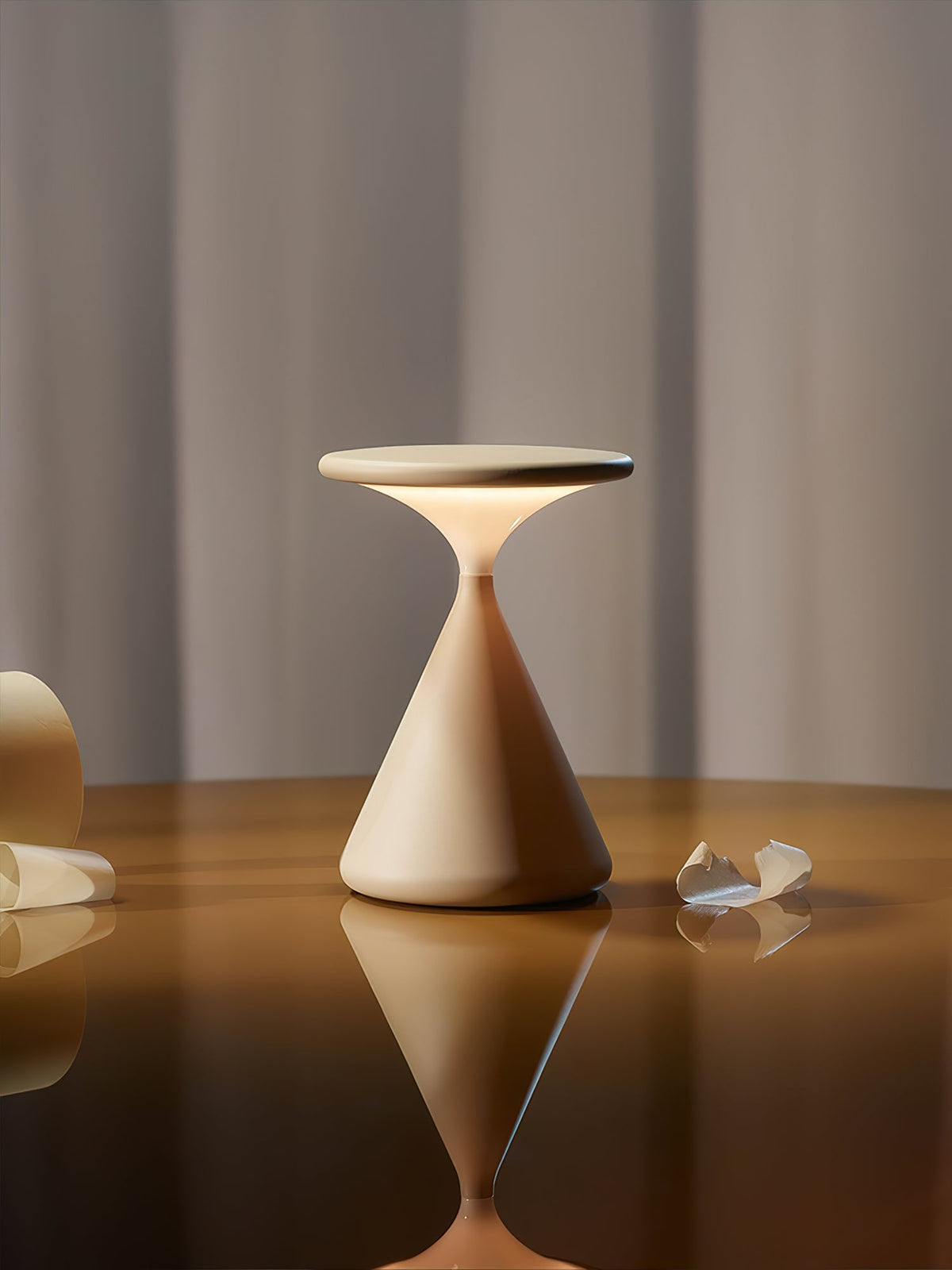 A cream Clérachic table lamp lit on a polished wooden table, with its reflection in the surface below.
