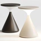 A black and a cream Clérachic table lamp side by side on a white backdrop, the cream one glowing at its waist.