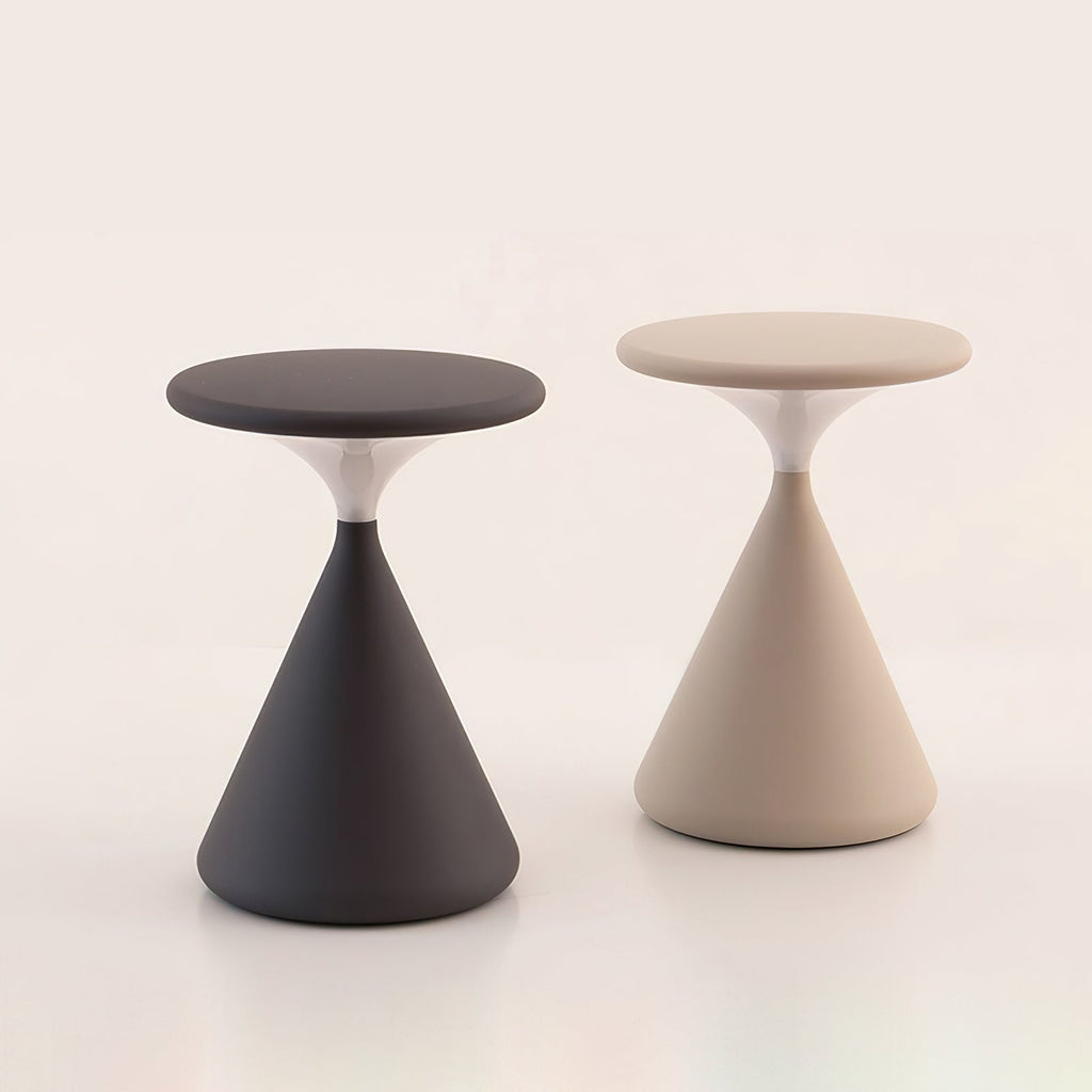 This Clérachic table lamp in black and in cream stands side by side, with flat disc tops and cone bases, on a pale backdrop.
