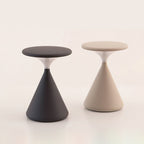 This Clérachic table lamp in black and in cream stands side by side, with flat disc tops and cone bases, on a pale backdrop.