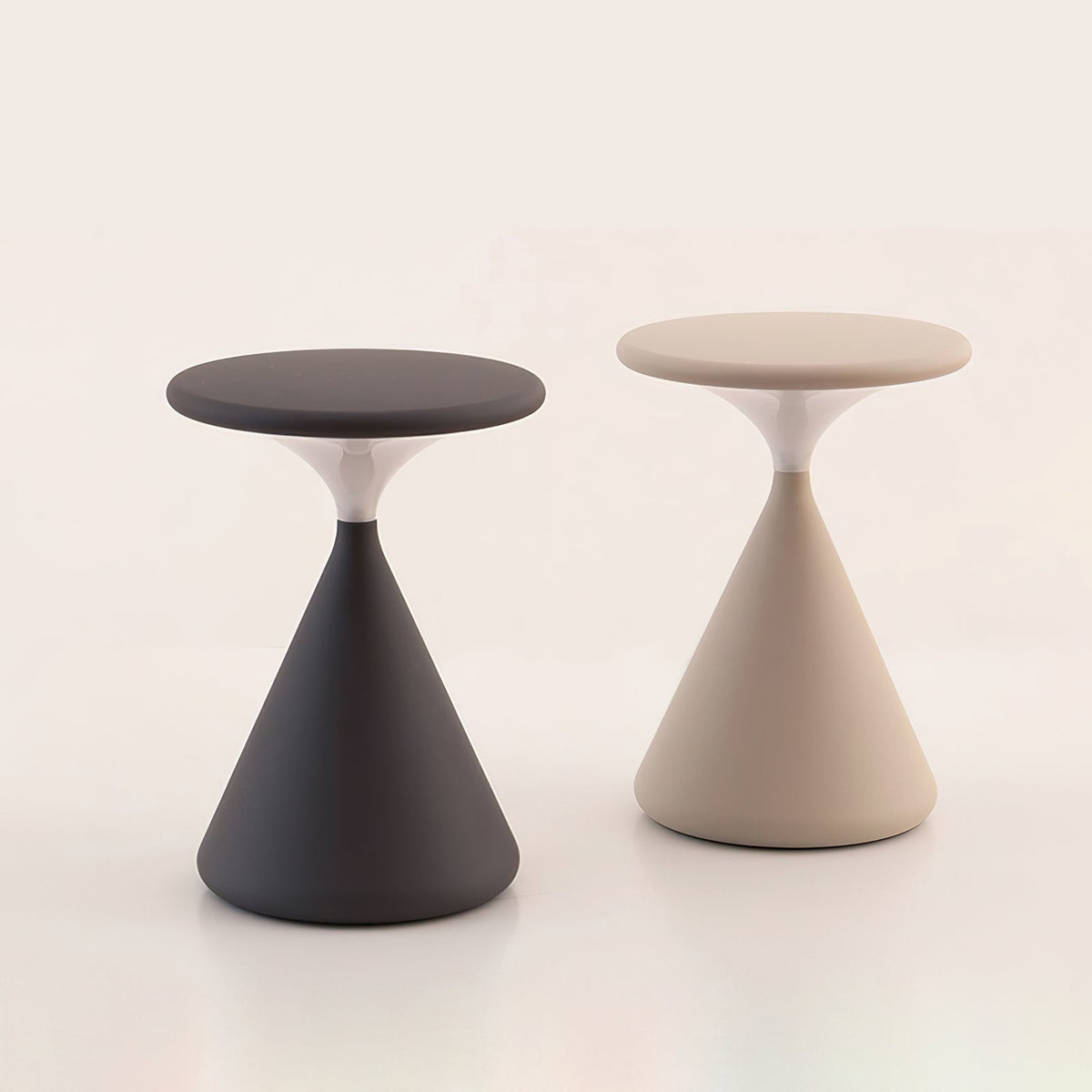 This Clérachic table lamp in black and in cream stands side by side, with flat disc tops and cone bases, on a pale backdrop.