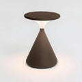 Brown Clérachic table lamp lit on a white backdrop, with a soft pool of warm light on the surface around its base.