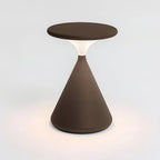 Brown Clérachic table lamp lit on a white backdrop, with a soft pool of warm light on the surface around its base.