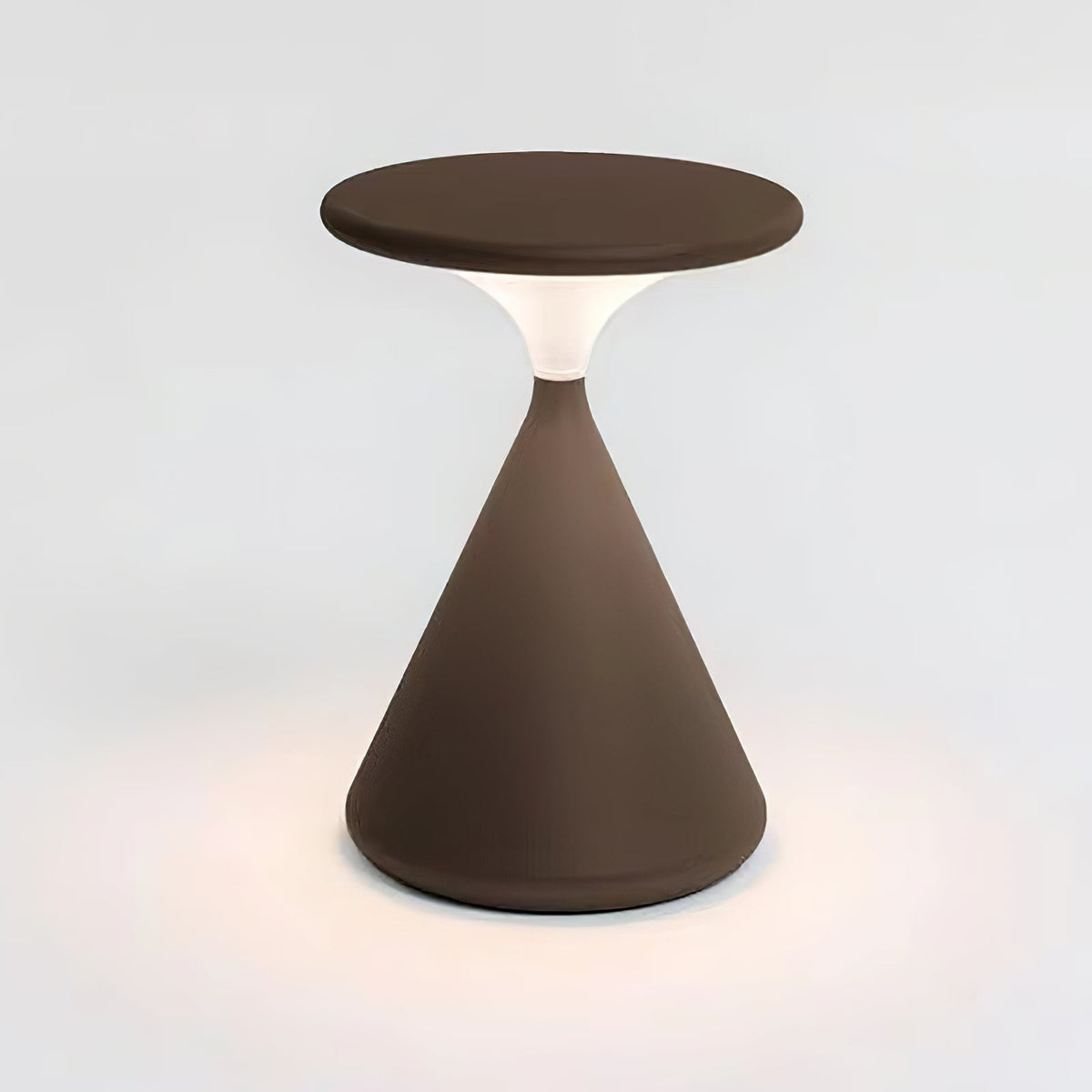 Brown Clérachic table lamp lit on a white backdrop, with a soft pool of warm light on the surface around its base.