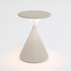 Cream Clérachic table lamp lit on a pale backdrop, with a soft warm glow around the base and under the disc top.