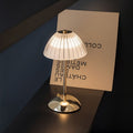 Clérachic cordless table lamp with a ribbed frosted dome shade and gold stem, glowing warm on a dark ledge.