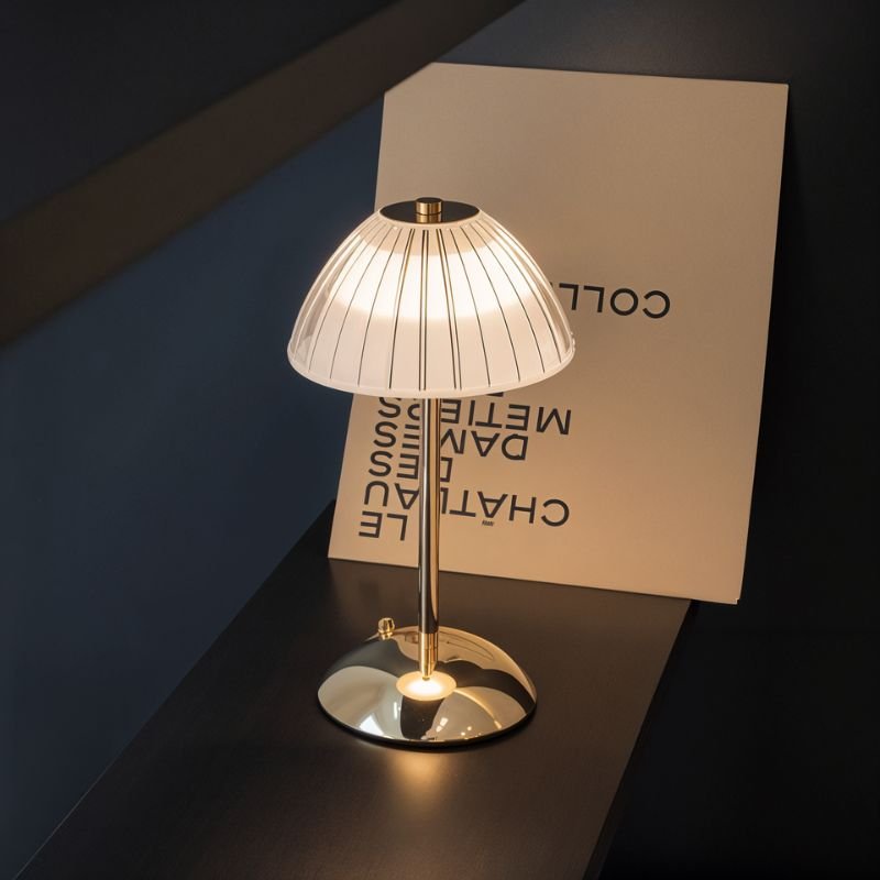 Clérachic cordless table lamp with a ribbed frosted dome shade and gold stem, glowing warm on a dark ledge.