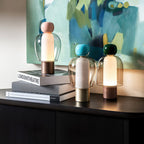 Three Clérachic table lamps of different heights on a black cabinet beside stacked books, in front of a blue-green painting.