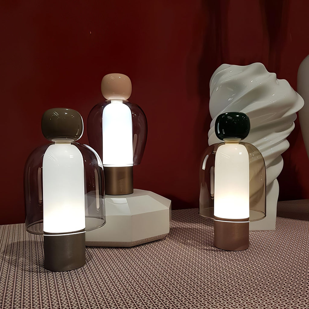 Three Clérachic table lamps glowing in front of a deep red wall, standing on a patterned cloth beside a white sculpted vase.