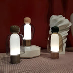 Three Clérachic table lamps glowing in front of a deep red wall, standing on a patterned cloth beside a white sculpted vase.