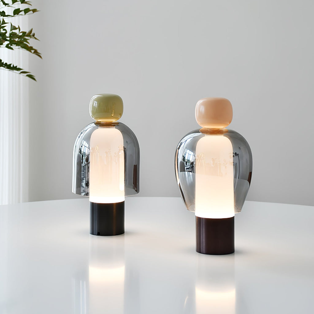 Two lit Clérachic table lamps on a white round table, one with an olive cap and one with a peach cap, against a pale wall.