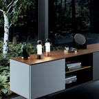 Two Clérachic table lamps lit on a pale cabinet with a wood top, with birch trunks and ferns visible through the window behind.
