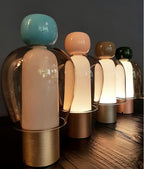 Four Clérachic table lamps in graduated heights on a dark wood surface, from a turquoise cap to a dark green one at the back.
